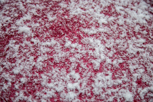 红色金属表面上雪花的背景。汽车引擎盖上有许多雪花图片下载