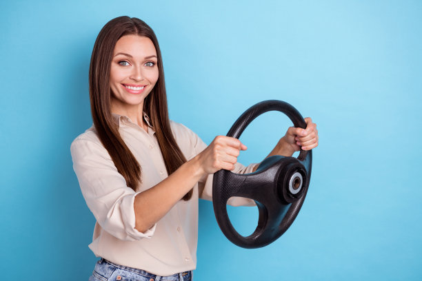 照片的狂喜漂亮可爱的女孩女士持有方向盘驱动站空空间孤立的蓝色背景图片下载