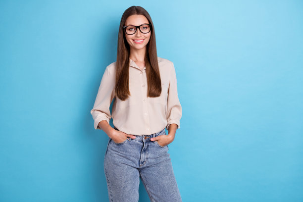 照片漂亮漂亮的女孩长发穿衬衫手臂在口袋站自信的姿势孤立在蓝色的背景图片下载
