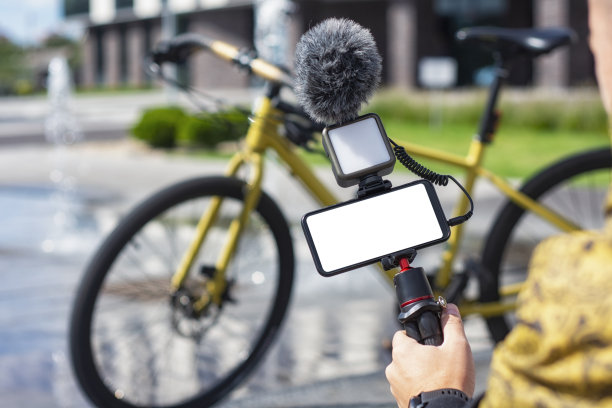 一名男博主手里拿着三脚架，自行车的背景是一个白色屏幕和带麦克风的灯的智能手机模型。图片下载