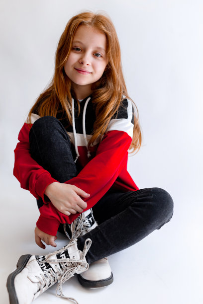 可爱的小女孩，红色的卷发，穿着时髦的坐在白色的背景图片下载