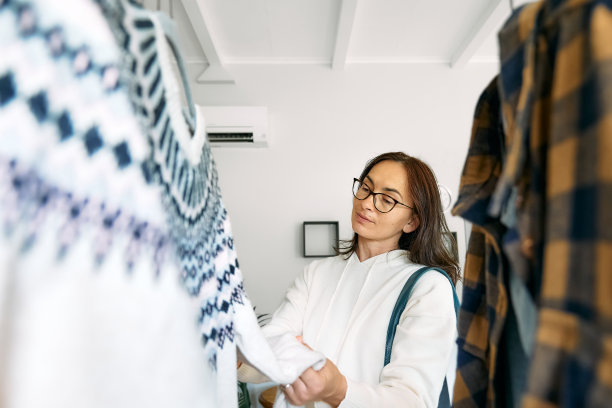 快乐的女人在商店买新衣服。针织毛衣挂在衣架的衣架上。慢时尚。有意识的消费。车库甩卖，再利用衣物，二手和生态消费理念图片下载