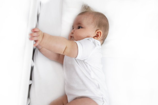 上面的照片是一个漂亮又平静的婴儿躺在她的婴儿床上，上面有干净的白色床单。图片下载