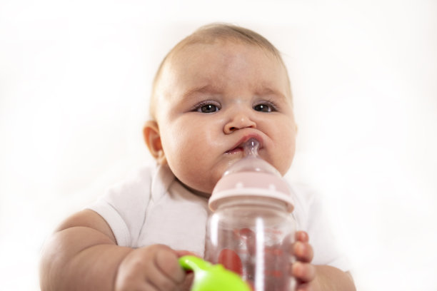 一张有趣的照片，一个婴儿看着相机，拿着他的奶瓶，有很多白色的拷贝背景。图片下载