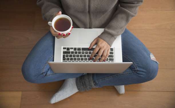 女人坐在木地板上，享受着一杯咖啡，在笔记本电脑上工作图片下载