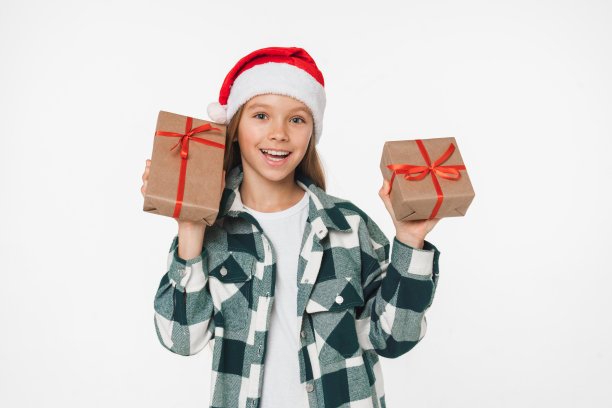 快乐的白人年轻前十几岁的少女在红色圣诞老人帽子摇晃圣诞新年礼物孤立在白色背景礼物图片下载