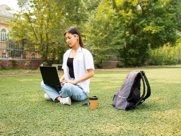 一位年轻的亚洲妇女坐在公园的草地上用笔记本电脑工作图片下载