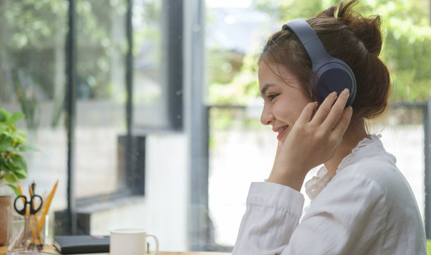 漂亮的年轻女子戴着无线耳机听音乐，在她的工作场所放松。图片下载