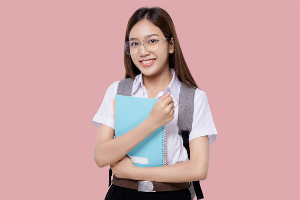 肖像微笑的十几岁的亚裔学生女孩在大学制服举行背包孤立的粉红色背景。图片下载