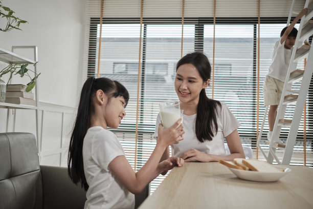 一位健康的亚洲母亲和女儿一起在餐桌上喝新鲜的牛奶。图片下载