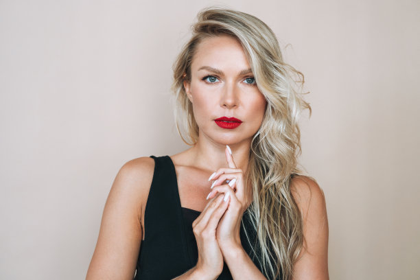 肖像华丽美丽的金发年轻女子与明亮的化妆在米色背景的晚礼服图片下载