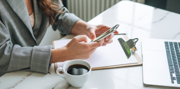 裁剪照片的女人长发在时尚的西装使用手机在明亮的现代办公室工作图片下载