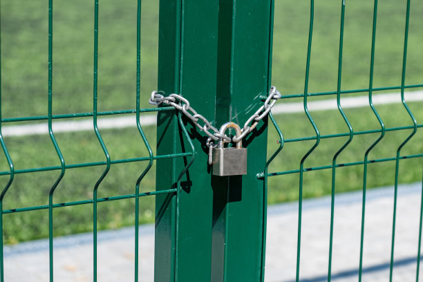 门上的锁生锈了。足球场的入口。背景是草的金属栅栏图片下载