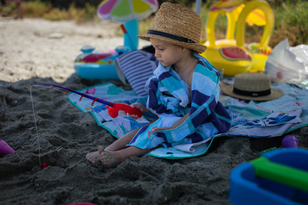 小女孩正坐在海滩上玩钓竿。图片下载