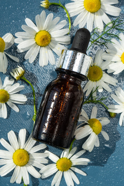 化妆品瓶与移液管和水滴在蓝色的背景与洋甘菊花。图片下载