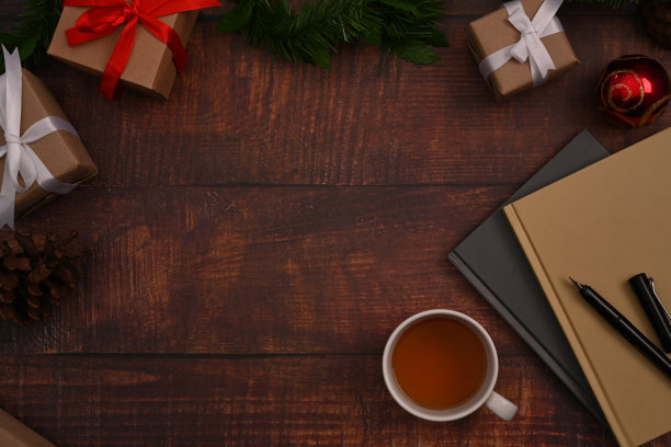 一个咖啡杯，笔记本，礼品盒，杉树树枝和松果在木制背景。圣诞背景的概念。图片下载