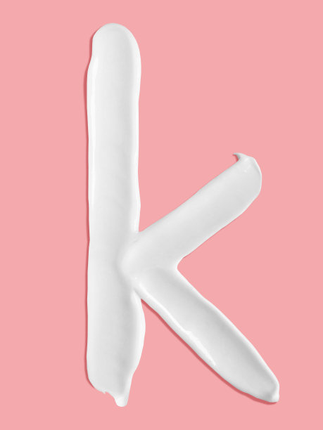 字母k，白色润肤霜涂抹笔画写在粉红色的背景，符号字母的一个字母图片下载