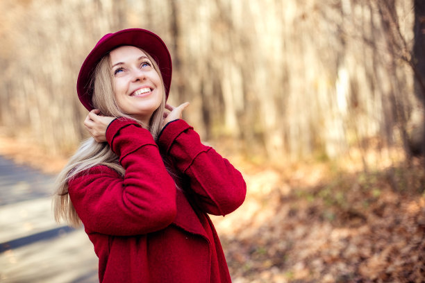 一个年轻迷人的女孩穿着红色的外套，戴着红色的帽子，走在秋天的森林里。图片下载