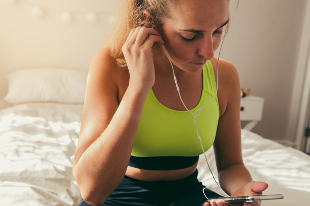 女士戴着耳机，在床上使用电话图片下载