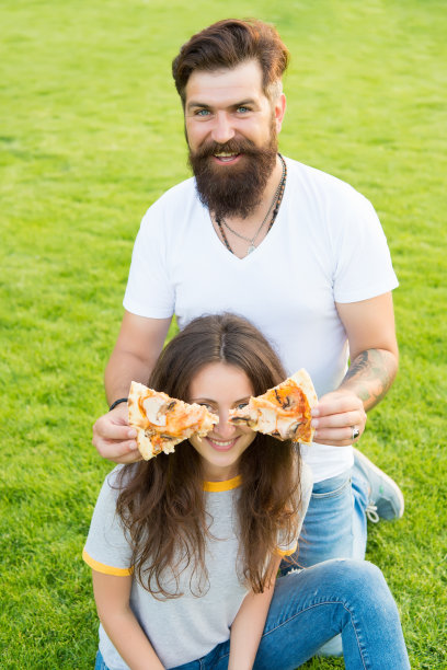 比萨蒙蔽。饥饿。家庭的周末。相爱的情侣约会。吃披萨的幸福夫妻。健康食品。快餐。大胡子潮男和美女一起吃披萨。在绿草地上的夏日野餐。饮食图片下载