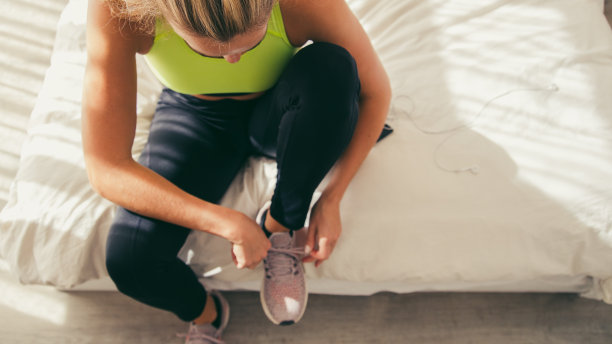 女跑步者在家里的床上系鞋带图片下载
