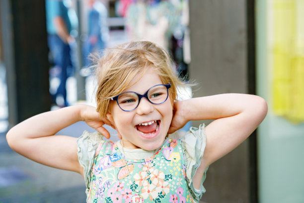 一个可爱的学龄前女孩的肖像与眼镜户外。快乐有趣的孩子戴着新的蓝色眼镜。城市里晴朗的夏日。图片下载