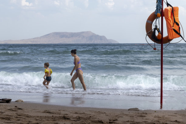 一个女人带着一个孩子在汹涌的大海中玩耍。图片下载