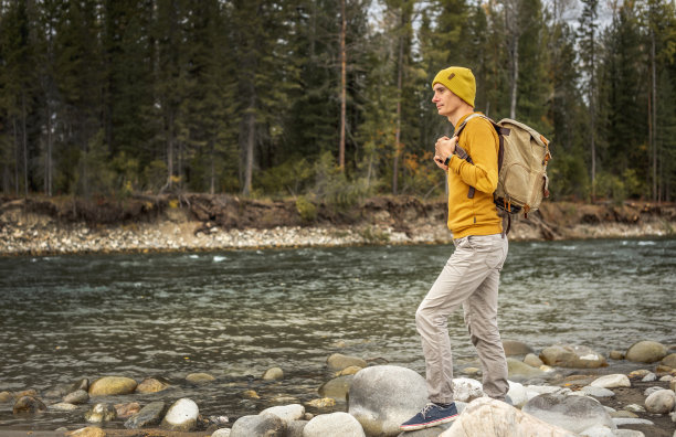 一个人沿着湍急的山间河流走着，河岸上有巨大的石头，背景是秋天的森林图片下载