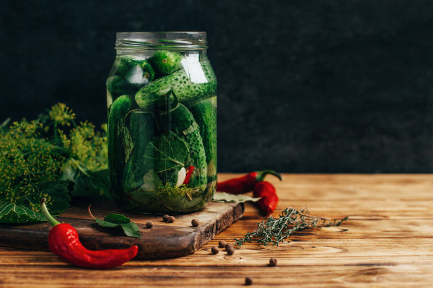 在深色背景的木桌上，一罐腌黄瓜配上青菜和胡椒调味料图片下载