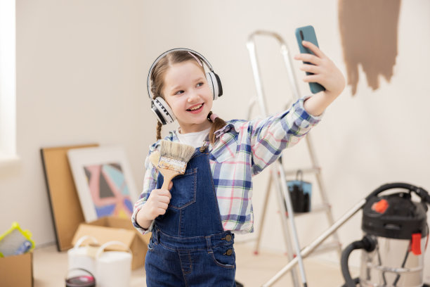 女孩博主向粉丝展示新房的装修情况。这个孩子耳朵上戴着耳机，左耳戴着电话，右耳拿着画笔。她非常高兴图片下载