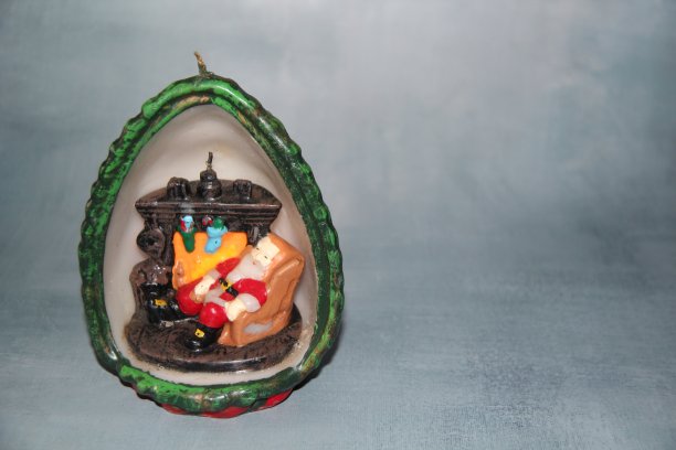 手工制作的蜡烛，里面的圣诞老人躺在壁炉旁边的扶手椅上。在灰色的背景和空白的文字。圣诞装饰。图片下载