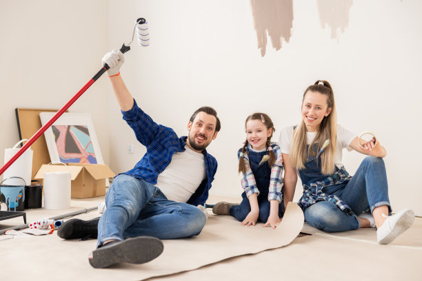 家人最近买了新公寓，已经开始装修。35岁的男人漂亮的金发女人和小女儿。父亲举起右手拿着油漆滚筒图片下载