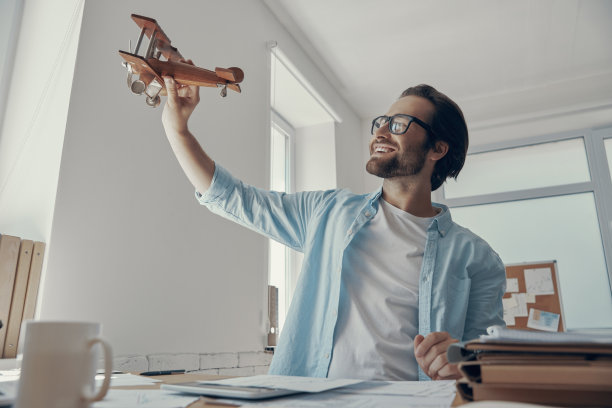 英俊的年轻人拿着木制飞机，微笑着坐在办公室里图片下载