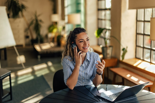 一个成年商业女孩坐在办公室里，在笔记本电脑前打电话。图片下载
