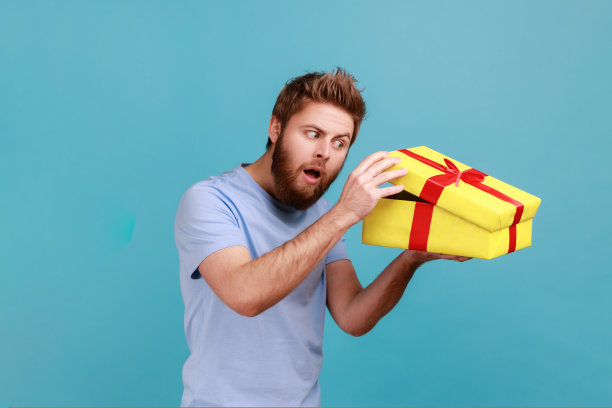 男子打开黄色礼品盒，带着好奇的表情看着里面，生日礼物。图片下载