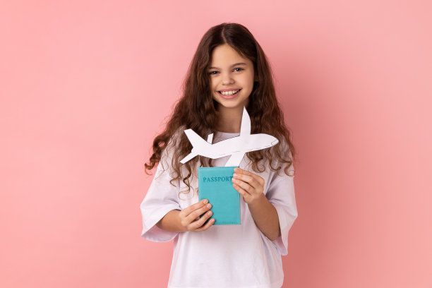 小女孩手里拿着护照和纸飞机，计划和父母一起去国外度假。图片下载