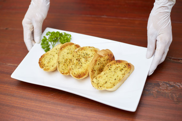 大蒜面包放在白色盘子里，餐厅服务员戴着白手套，以保证清洁和安全。图片下载