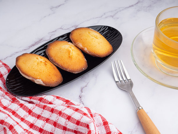 柠檬釉玛德琳蛋糕放在黑色的盘子里，一杯茶放在大理石背景和白色砖墙上图片下载