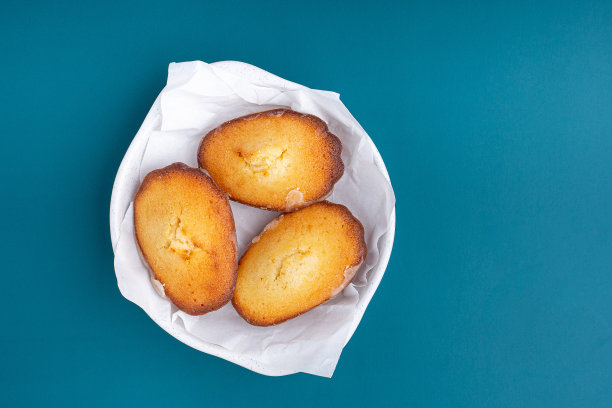 柠檬釉玛德琳蛋糕放在蓝色灯光背景的盘子里。图片下载