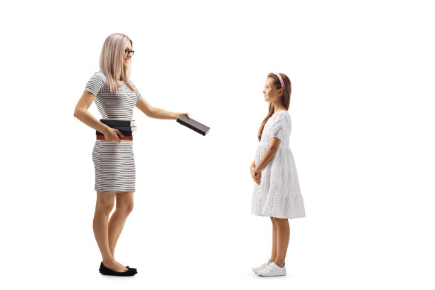 一个女人给一个穿白裙子的女孩一本书的完整的侧面镜头图片下载