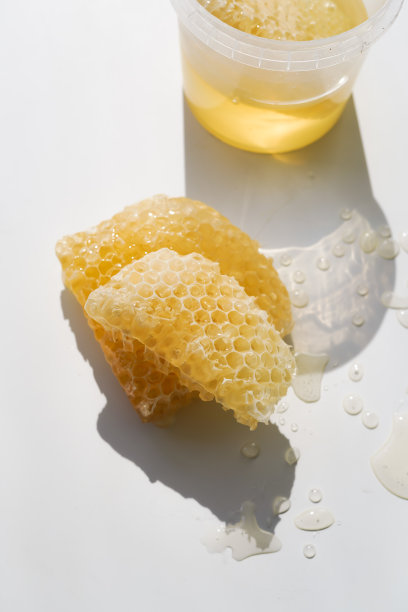 透明的新鲜蜂蜜的蜂巢躺在阳光下的光背景下，旁边是一个塑料透明容器的蜂蜜和蜂巢图片下载