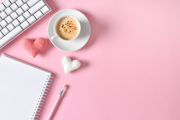 办公室办公桌的俯视图。浪漫的气氛。一个笔记本，上面有一杯咖啡、心形图案和一个粉色背景的键盘图片下载