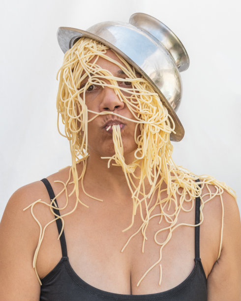 吃意大利面的女人头上戴着过滤器当帽子。饥饿的概念。图片下载
