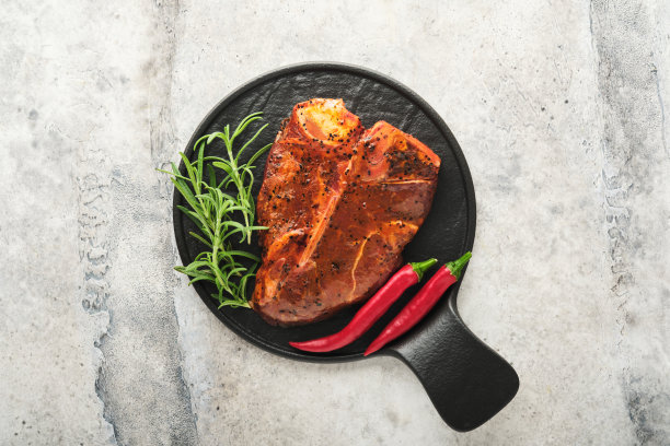 生牛排、t骨或上肉排。t骨牛排或上肉排配调味料、盐和迷迭香，放在混凝土背景的黑色陶瓷盘上。前视图。文本。图片下载