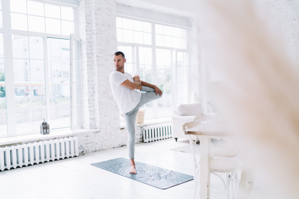 专注的白人男性单腿站立，保持平衡，享受感觉身体和专注力，积极的20多岁的潮人花空闲时间在公寓的地毯上进行瑜伽训练图片下载