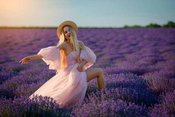 一个年轻美丽的快乐的微笑着的女人，穿着粉红色的衣服，戴着帽子走在薰衣草田的肖像图片下载