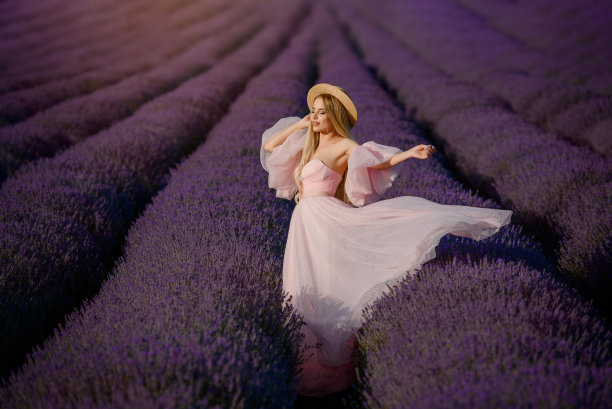 年轻漂亮的女人穿着粉红色的裙子，戴着帽子，走在薰衣草田。图片下载