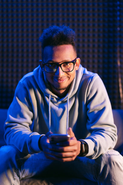 卷毛男人戴着眼镜，拿着智能手机坐在沙发上图片下载