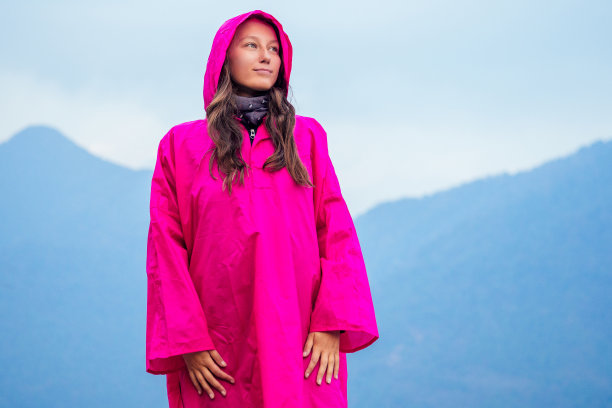 美丽年轻的女孩穿着粉红色的雨衣，背景是雨中的群山。山地活动休闲和旅游的概念。在尼泊尔喜马拉雅山徒步旅行图片下载