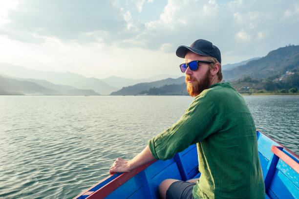 美丽的男子在湖上的船在山的背景。户外活动的概念和旅游的本质。在尼泊尔喜马拉雅山徒步旅行图片下载